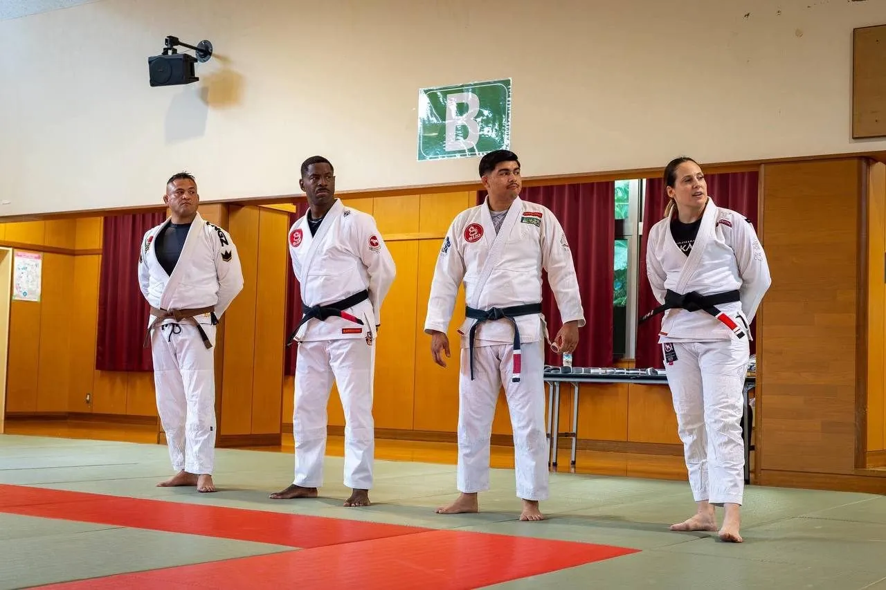 Four BJJO black belts lined up on the mats at a tournament venue